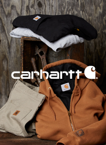 Image of a brown Carhartt zip-up hoodie, khaki work pants, a black t-shirt and gray t-shirt folded. The hoodie and pants are stood up against an open box with tools inside. The two t-shirts are laying on top. White text overlay of the Carhartt logo.