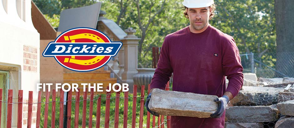 Image of a man carrying a large rock outside and wearing a hard hat. The Dickies logo and 